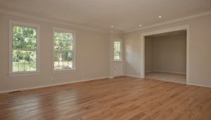 Vacant room with newly laid light hardwood flooring, beige walls, and three windows before any trade enters